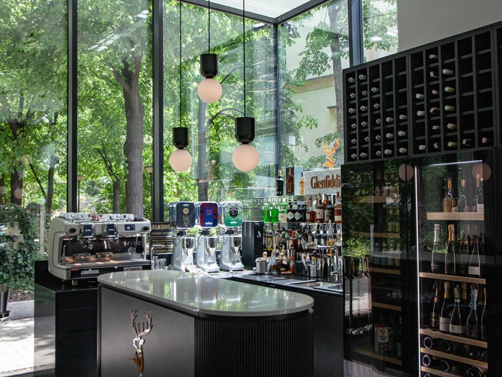 nuta restaurant in warsaw interior bar with wine fridge and coffee maker pendant lighting and large windows with view onto greenery and trees